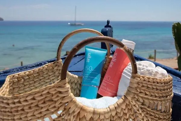 a beach bag holding two saltee SPFs on a beach with the sea in the background